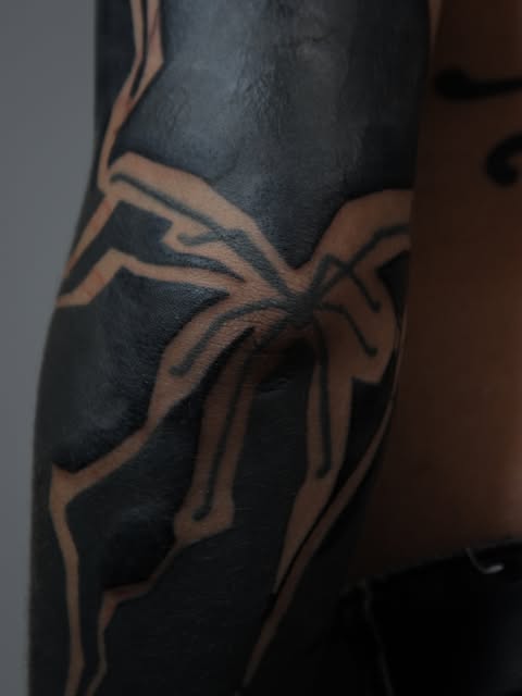 Heavy blackwork arm tattoo with negative-space lines by Zuzana Mala